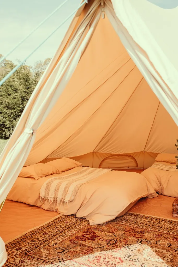 Inside a furnished bell tent with peach bedding and a patterned rug at Woodhill Campsite, Faversham, Kent