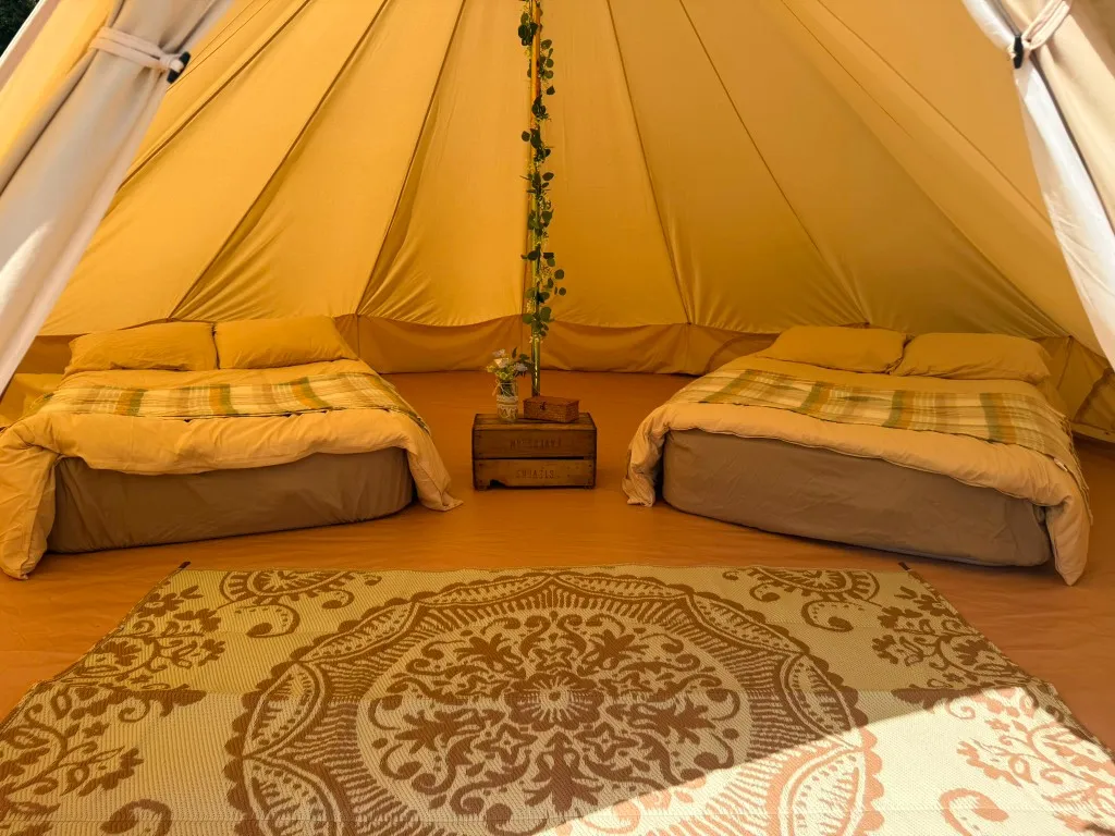 A two-bed bell tent interior with plaid throws and a floral crate table at Woodhill Campsite, Faversham, Kent