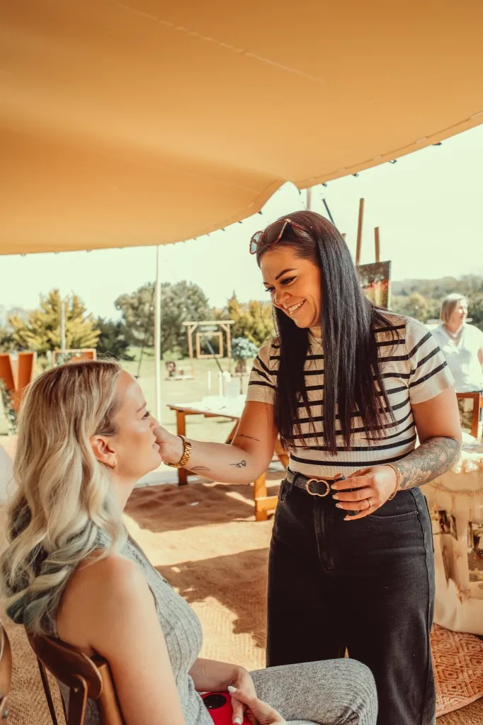 Emma applying a bride’s makeup under the stretch tent on the morning of the wedding