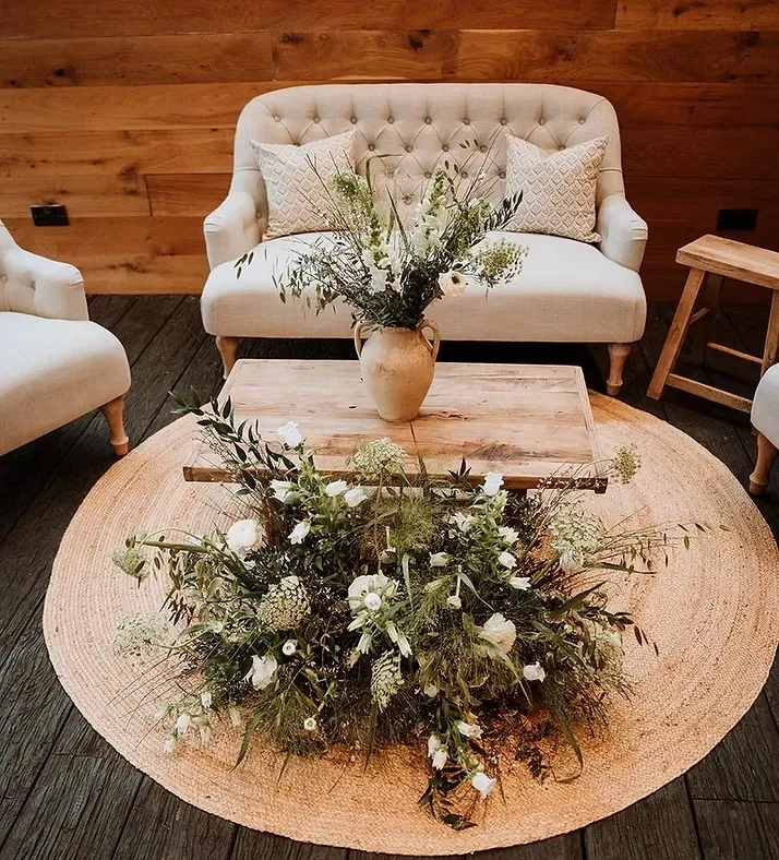 A rustic-luxe lounge setup with cream tufted seating, a reclaimed wood coffee table and wild floral arrangements by Locate To Create