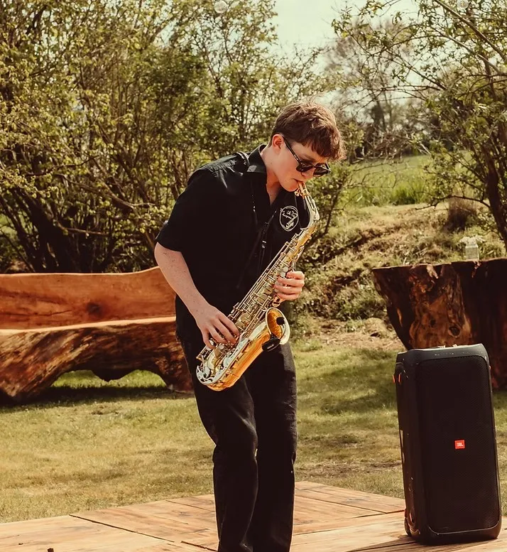 Owen playing saxophone outdoors at a wedding with a portable speaker beside him