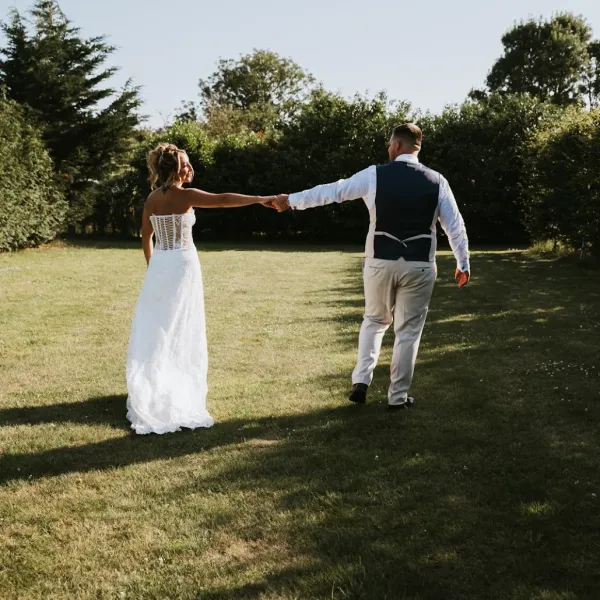 A bride and groom walking hand in hand across the lawn at Woodhill Weddings, Faversham, Kent