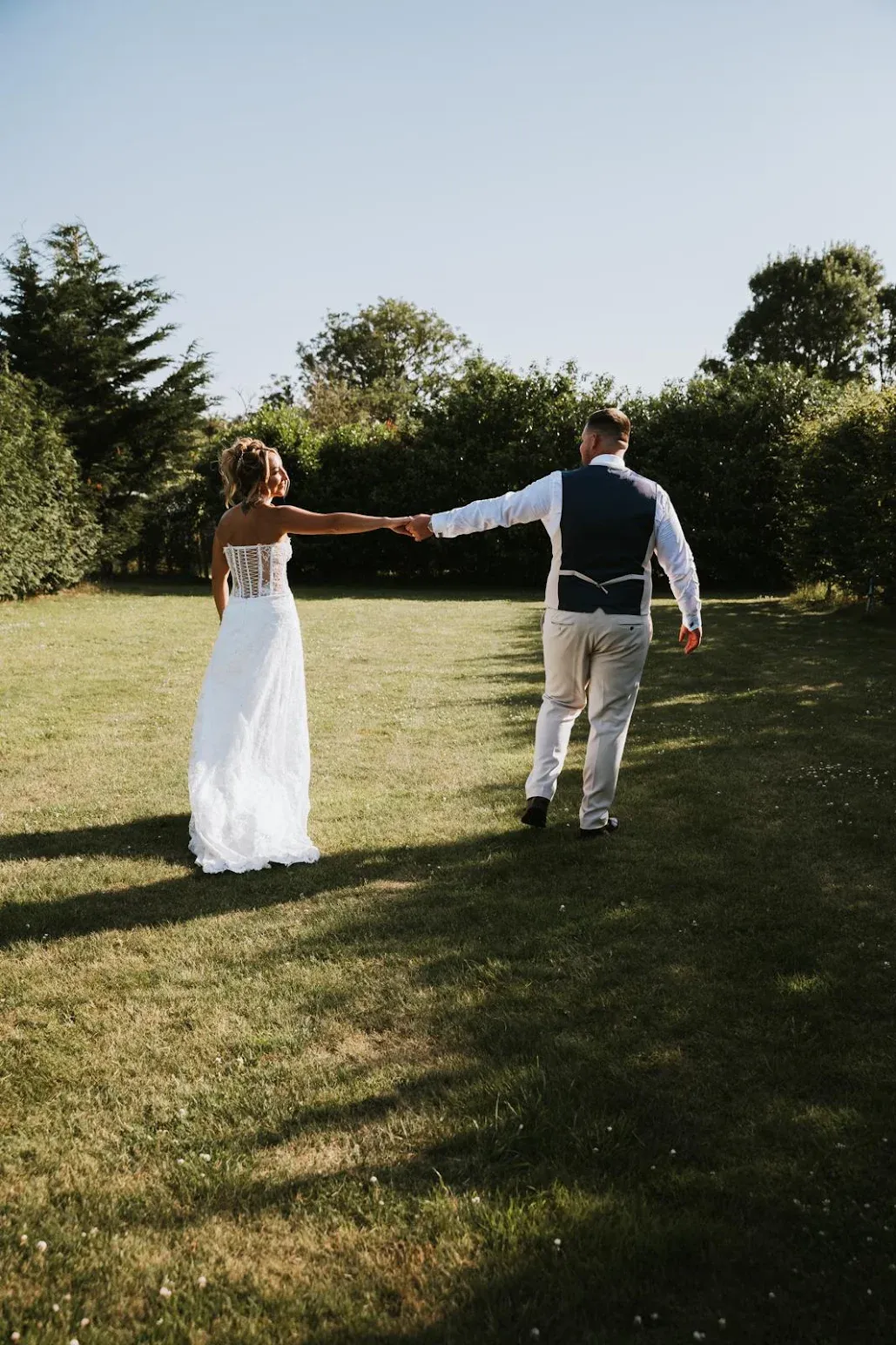 A bride and groom walking hand in hand across the lawn at Woodhill Weddings, Faversham, Kent