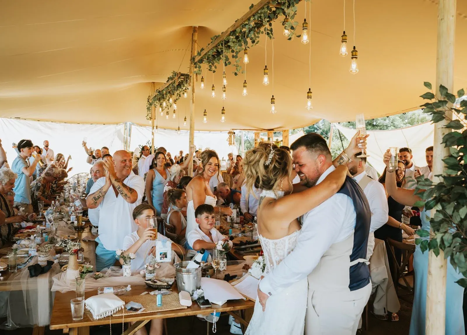A newlywed couple embrace as their guests cheer under the Bedouin stretch tent at Woodhill Weddings, Faversham, Kent