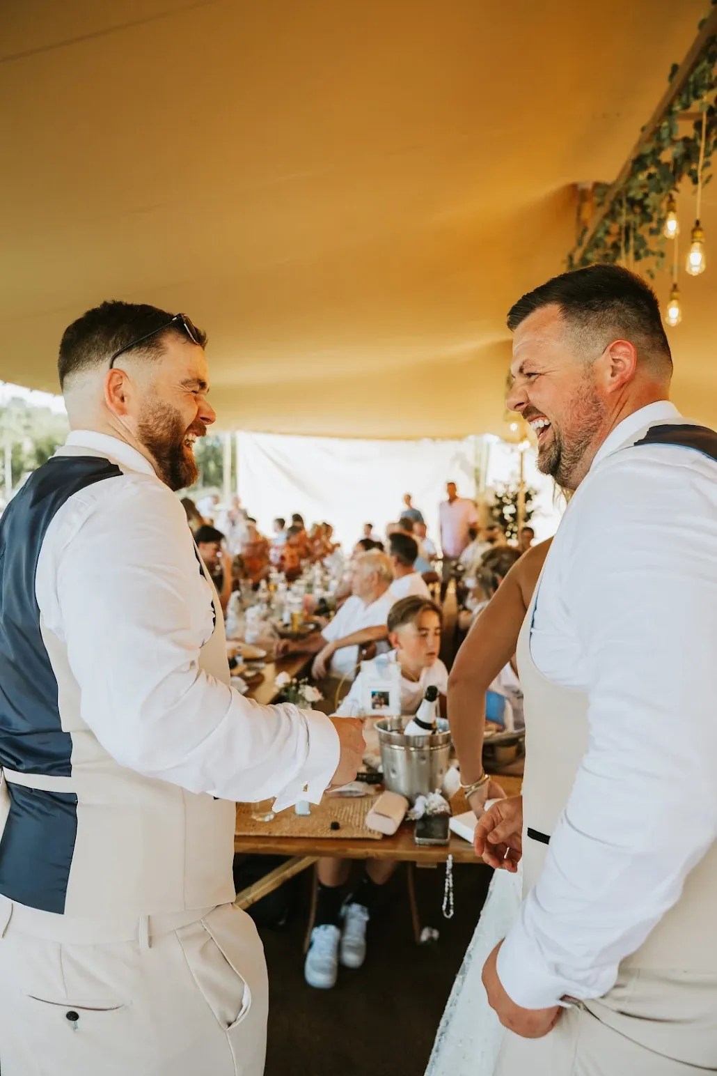 The groom sharing a laugh with a guest under the stretch tent during the wedding breakfast at Woodhill Weddings, Faversham, Kent