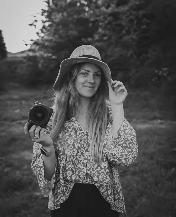 Molly of Wild Meadow Photography holding a camera outdoors in a meadow, wearing a sun hat